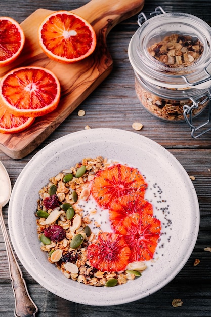 Petit-déjeuner sain bol de granola fait maison avec du yogourt frais et des tranches de sang oranges sur fond de bois