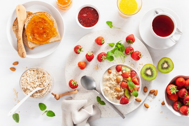 Petit-déjeuner sain avec de la bouillie d'avoine, des fraises, des noix, du pain grillé, de la confiture et du thé. Vue de dessus