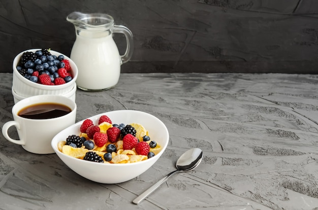 Petit-déjeuner sain avec des cornflakes dans une assiette blanche, des baies, du lait et du café