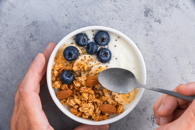 Petit-déjeuner sain avec du yogourt granola fruits noix et graines de chia Mains mâles tenant une cuillère au-dessus d'un bol de petit-déjeuner