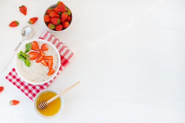 Petit déjeuner sain et équilibré de flocons d'avoine avec des fraises et du miel sur un mur blanc. Photo horizontale avec espace de copie. Vue de dessus