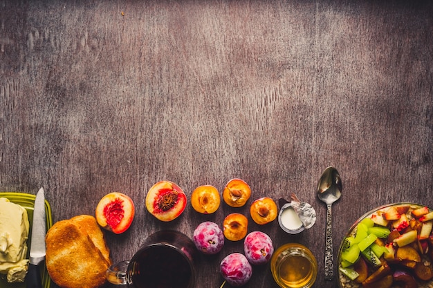 Petit-déjeuner sain avec de la farine d'avoine dans un bol en verre, des prunes, du miel, de la crème et une tasse de thé noir sur fond de bois foncé. Vue de dessus. Espace de copie. Nature morte. Mise à plat. tonique