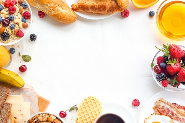 Petit-déjeuner sain avec des fruits, des baies, des noix, du café, des œufs, du miel et des céréales sur fond blanc