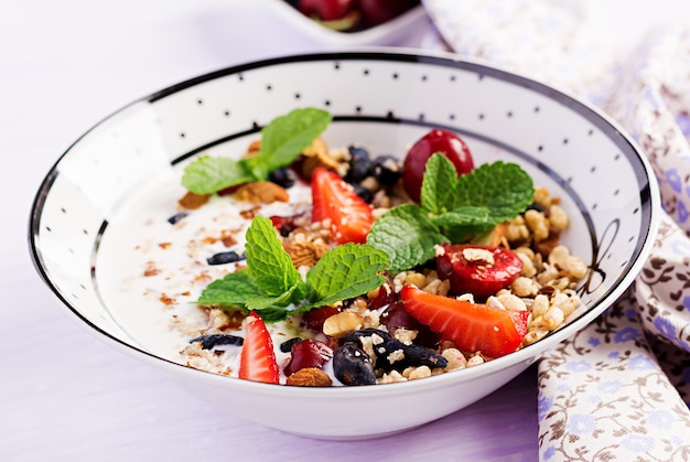 Petit déjeuner sain - granola, fraises, cerise, baie de chèvrefeuille, noix et yaourt dans un bol. Concept alimentaire végétarien.