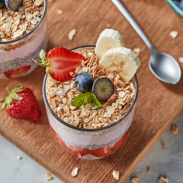 Petit-déjeuner sain avec granola maison, yaourt, tranches de fraises, banane, myrtilles, flocons d'avoine, graines de chia sur une planche en bois. Concept de régime alimentaire sain.