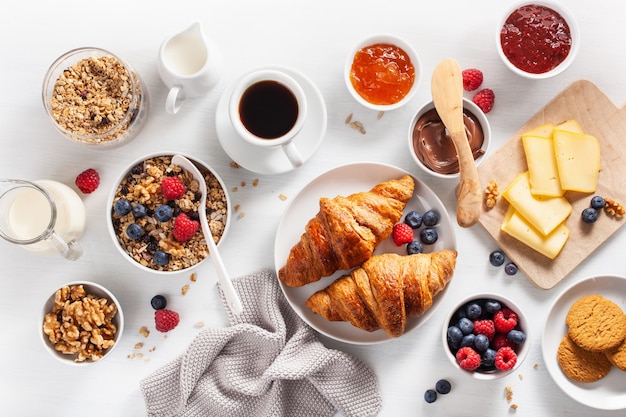 Petit-déjeuner sain avec granola, petits fruits, noix, croissant, confiture, pâte à tartiner au chocolat et café. Vue de dessus