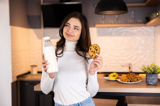 Petit-déjeuner sain - heureuse belle femme, boire du lait et manger des biscuits dans la cuisine.