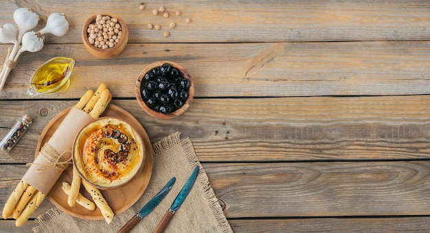 Petit-déjeuner sain avec houmous maison, olives noires et pain croustillant sur une surface en bois. Régime alimentaire et collation saine.