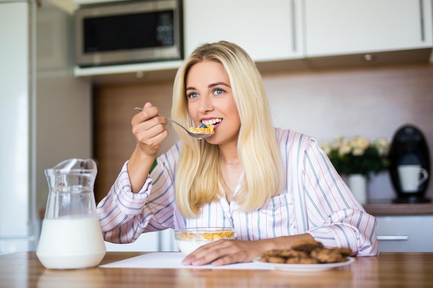 Petit déjeuner sain - jeune belle femme gaie mangeant des flocons de maïs avec du lait à la maison