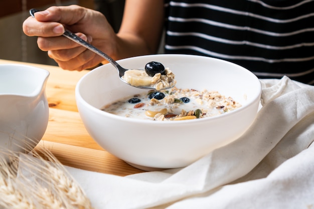 Petit-déjeuner sain. Jeune femme asiatique, manger du granola frais, du muesli avec du lait et des baies sur fond de table en bois.