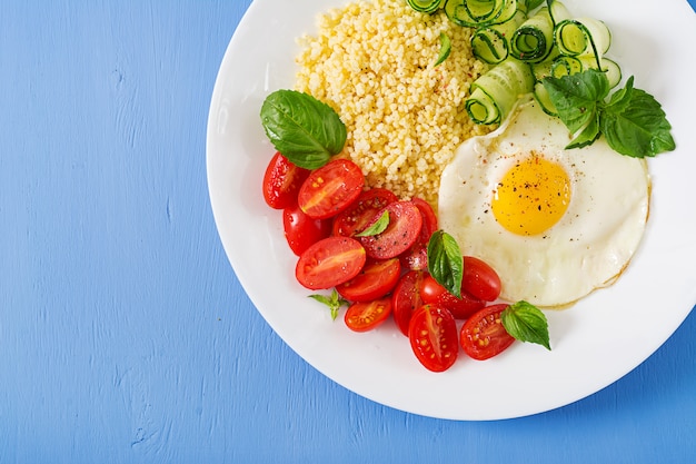 Petit-déjeuner sain. Menu diététique. Bouillie de millet et tomate, salade de concombre et œufs au plat. Vue de dessus. Mise à plat