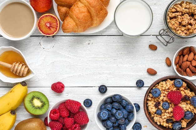 Petit-déjeuner sain avec muesli granola, fruits, baies, noix, croissant et tasse de café