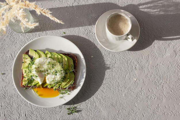 Petit-déjeuner sain pain de grains entiers grillés avec microgreens d'œufs pochés à l'avocat et une tasse de café