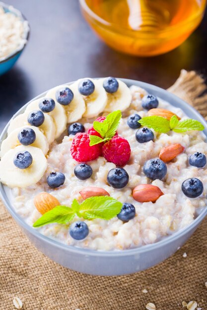 Photo petit-déjeuner sain porridge d'avoine avec des baies, des fruits et du miel sur un fond sombre