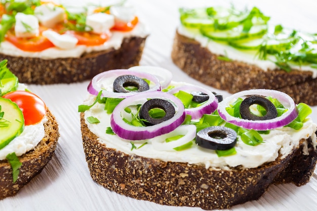 Photo petit-déjeuner sain: sandwiches au fromage à la crème et aux légumes sur une table en bois blanche