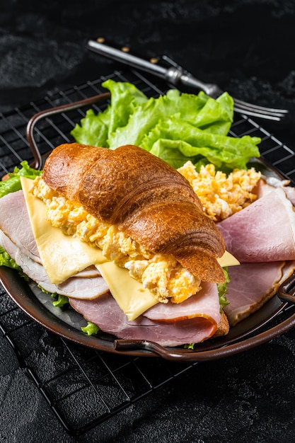 Petit-déjeuner sandwich croissant avec fromage oeufs brouillés et jambon Fond noir Vue de dessus