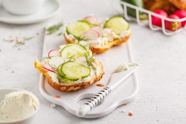 Petit déjeuner sandwichs au fromage à la crème, concombre et radis sur un tableau blanc.