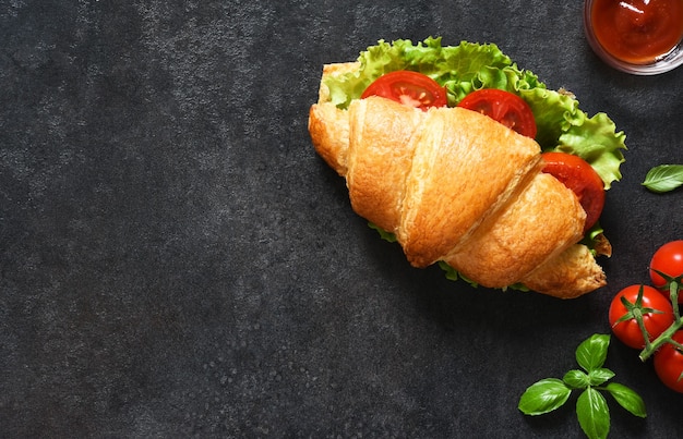 Petit-déjeuner avec des sandwichs croissants avec des feuilles de salade, du jambon et des tomates cerises, avec une sauce sur fond noir. Vue d'en-haut.