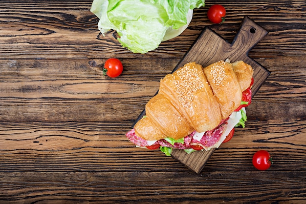 Petit déjeuner savoureux. Croissant appétissant au salami et au fromage et aux tomates. Mise à plat. Vue de dessus