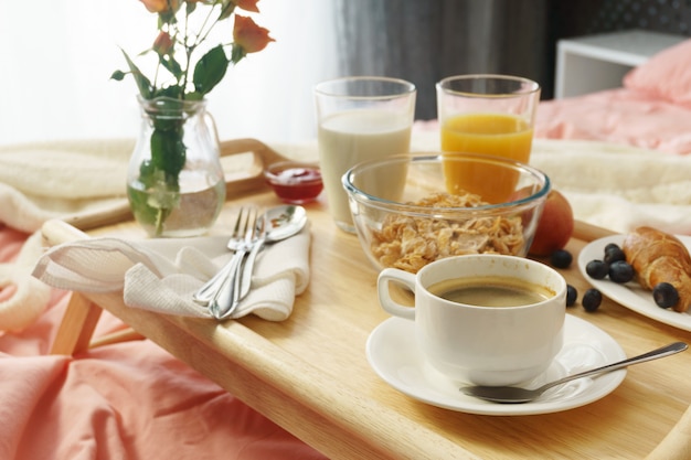 Petit déjeuner servi au lit sur un plateau en bois avec café et croissants