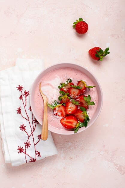 Petit-déjeuner avec smoothie granola, noix de coco et fraise dans un bol sur fond rose clair. Menu de régime de printemps. Vue de dessus.