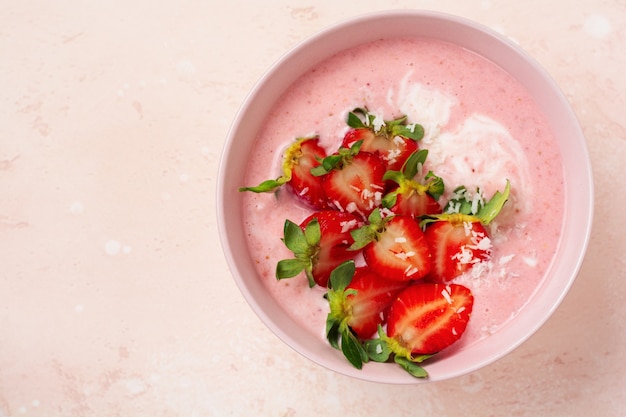 Petit-déjeuner avec smoothie granola, noix de coco et fraise dans un bol sur un mur de lumière rose. Menu de régime de printemps Vue de dessus.