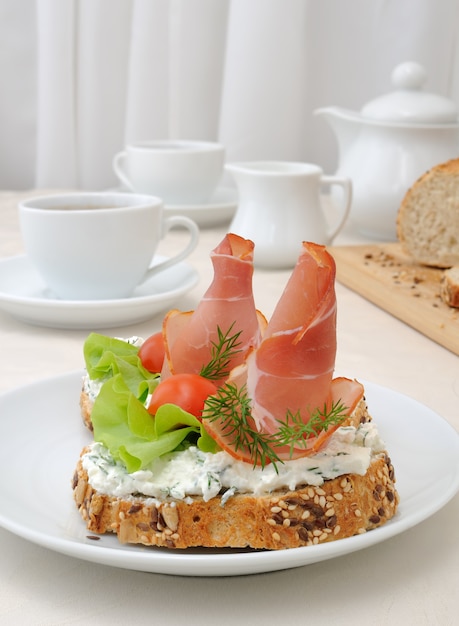 Petit-déjeuner avec une tasse de café et un sandwich de pain de grains entiers à la ricotta et au jambon