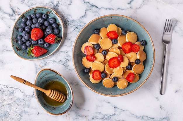 Petit-déjeuner tendance avec mini crêpes, myrtilles et fraises, vue de dessus.