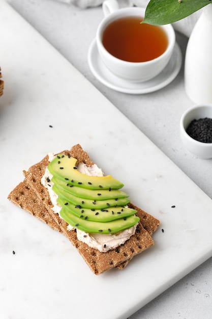 Petit-déjeuner avec toast à l'avocat avec pain complet aux graines de sésame noir sur planche de marbre. Tasse de thé.