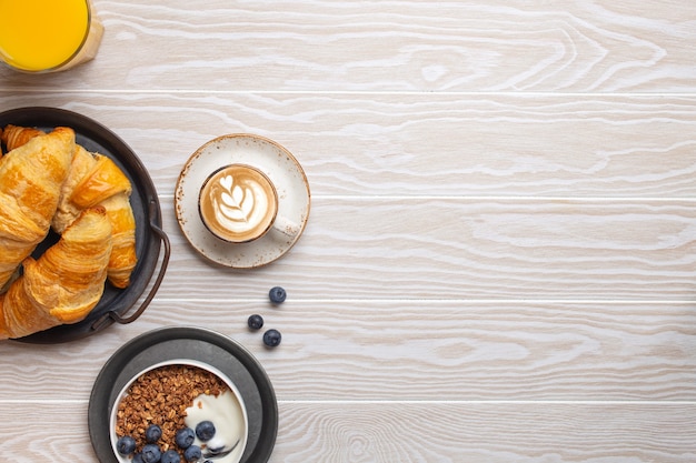 Petit-déjeuner traditionnel du matin sur fond de bois blanc rustique. Croissants frais, granola avec yaourt et baies, café cappuccino et jus d'orange. Réglage du petit-déjeuner, espace pour le texte