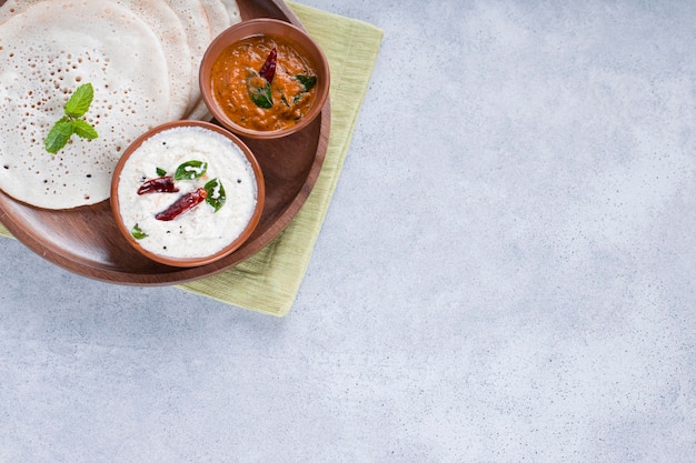 Petit-déjeuner traditionnel du sud de l'Inde Dosa ou Thattu dosa à base de dosa thawa en fonte disposés dans une vaisselle avec accompagnement chutney de noix de coco blanche et chutney d'oignons sur fond blanc texturé