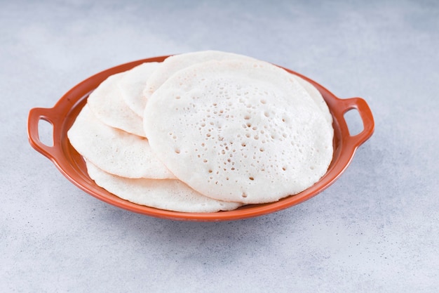 Photo petit-déjeuner traditionnel du sud de l'inde dosa ou thattu dosa fait à l'aide de dosa thawa en fonte disposé dans une vaisselle qui est placée sur un fond texturé blanc