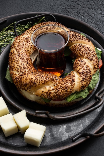 Petit-déjeuner turc rapide Simit avec du fromage et des légumes avec un verre de thé noir turc avec un verre de thé noir turc sur fond de table en pierre noire foncée