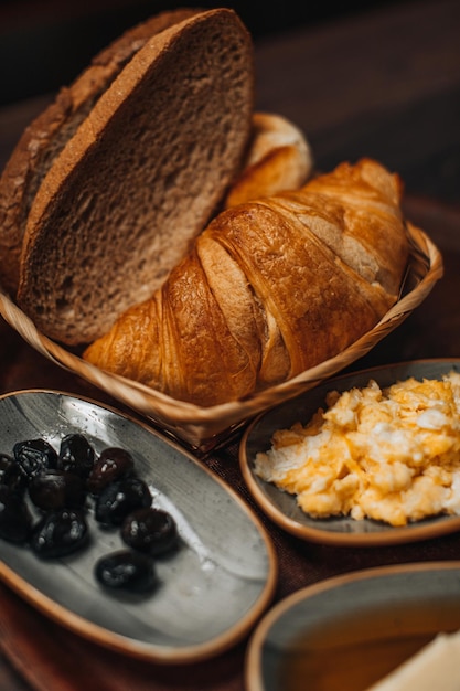 Petit-déjeuner turc traditionnel avec œuf au plat, olives noires, croissant, pain, fromage, beurre au miel et thé sur une table en bois. Cuisine bio, fraîche et savoureuse. Verticale