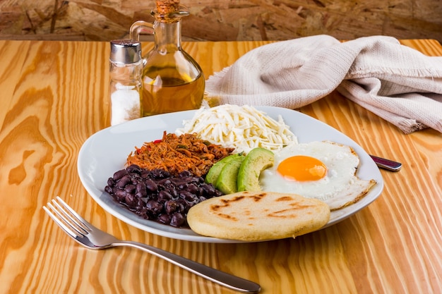 Petit déjeuner vénézuélien d'arepa, oeuf au plat, haricots noirs, viande de mechada, fromage blanc et avocat