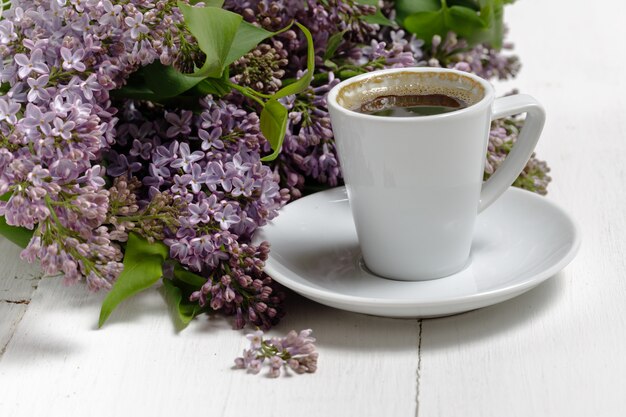 Petit délicat bouquet élégant de fleurs de printemps et une tasse de thé sur une table en bois blanc, petit déjeuner le matin