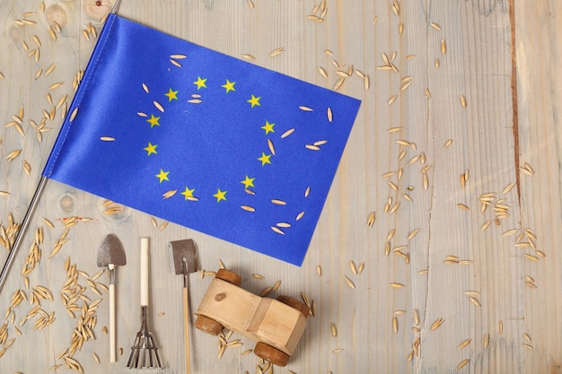 Petit drapeau de l'Union européenne et des grains d'avoine, outils agricoles, tracteur jouet en bois sur une surface en bois. Espace libre pour un texte