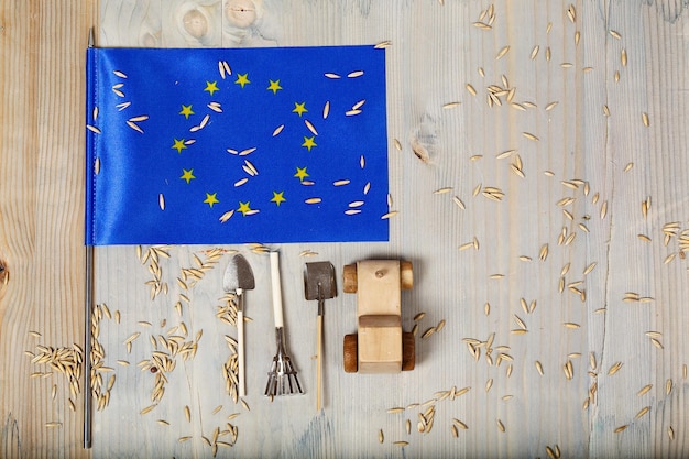 Petit drapeau de l'Union européenne et des grains d'avoine, outils agricoles, tracteur jouet en bois sur une surface en bois. Espace libre pour un texte