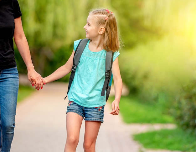 Petit écolier marchant main dans la main avec sa mère dans un parc ensoleillé