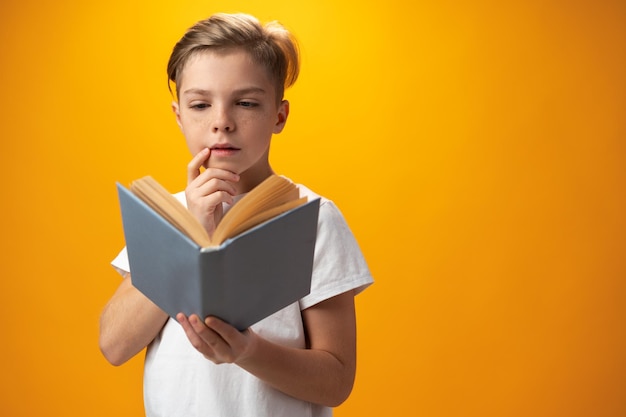 Petit écolier tenant un livre sur fond jaune