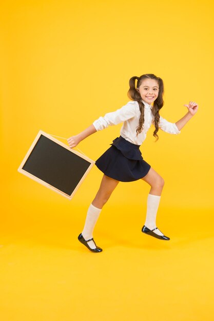 Petit et énergique Petit enfant portant un tableau noir sur fond jaune Petite écolière avec tableau noir pour la publicité de l'école Petite fille avec tableau vide pour votre espace de copie de texte