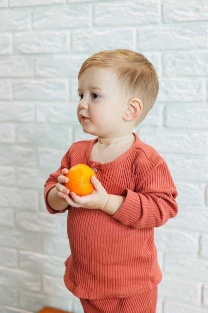 Un petit enfant de 2 ans tient un agrume orange dans ses mains Le garçon veut manger de la mandarine