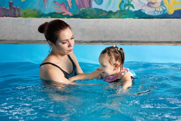 Petit enfant apprenant à nager dans la piscine avec un professeur