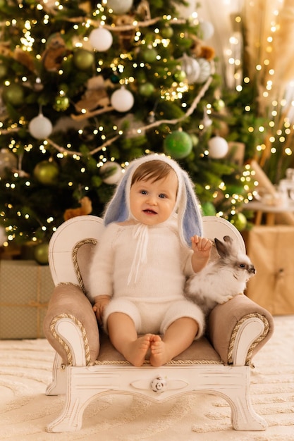 petit enfant avec arbre de Noël bébé est assis avec un lapin sur une chaise à l'arrière-plan au C