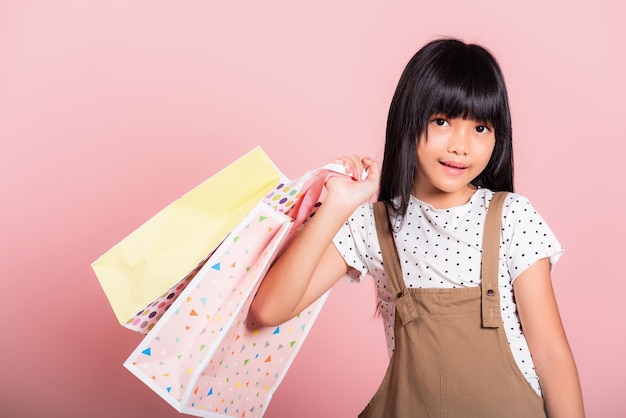 Petit enfant asiatique de 10 ans souriant tenant des sacs à provisions multicolores dans les mains