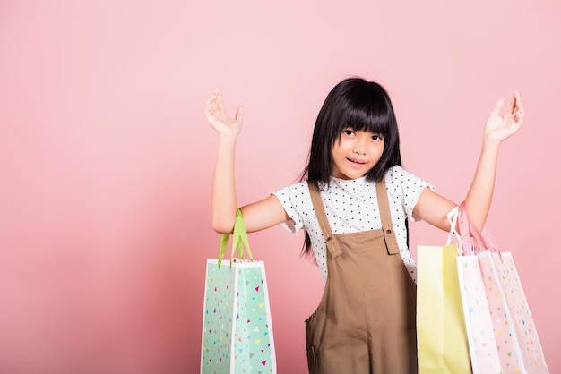 Petit enfant asiatique de 10 ans souriant tenant des sacs à provisions multicolores dans les mains