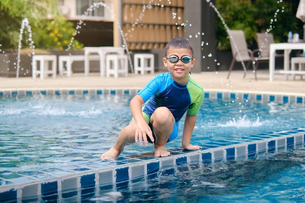 Petit enfant asiatique en lunettes de natation et maillot de bain apprenant à nager à la piscine extérieure en été