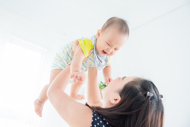 Petit enfant asiatique sourit joyeusement tout en jouant avec la mère dans le salon