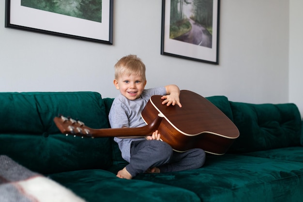 Petit enfant aux cheveux blonds jouant de la guitare à la maison