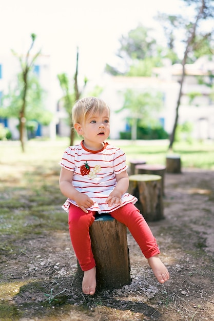 Le petit enfant aux pieds nus s'assied sur une souche d'arbre